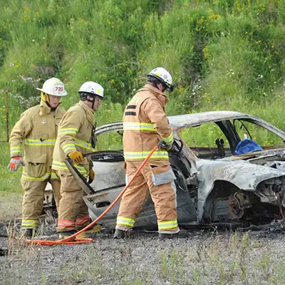 fire fighters assess burned out car in open field